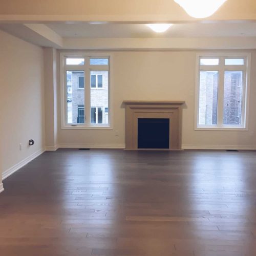 An empty living room with a fireplace and newly installed flooring in a new house